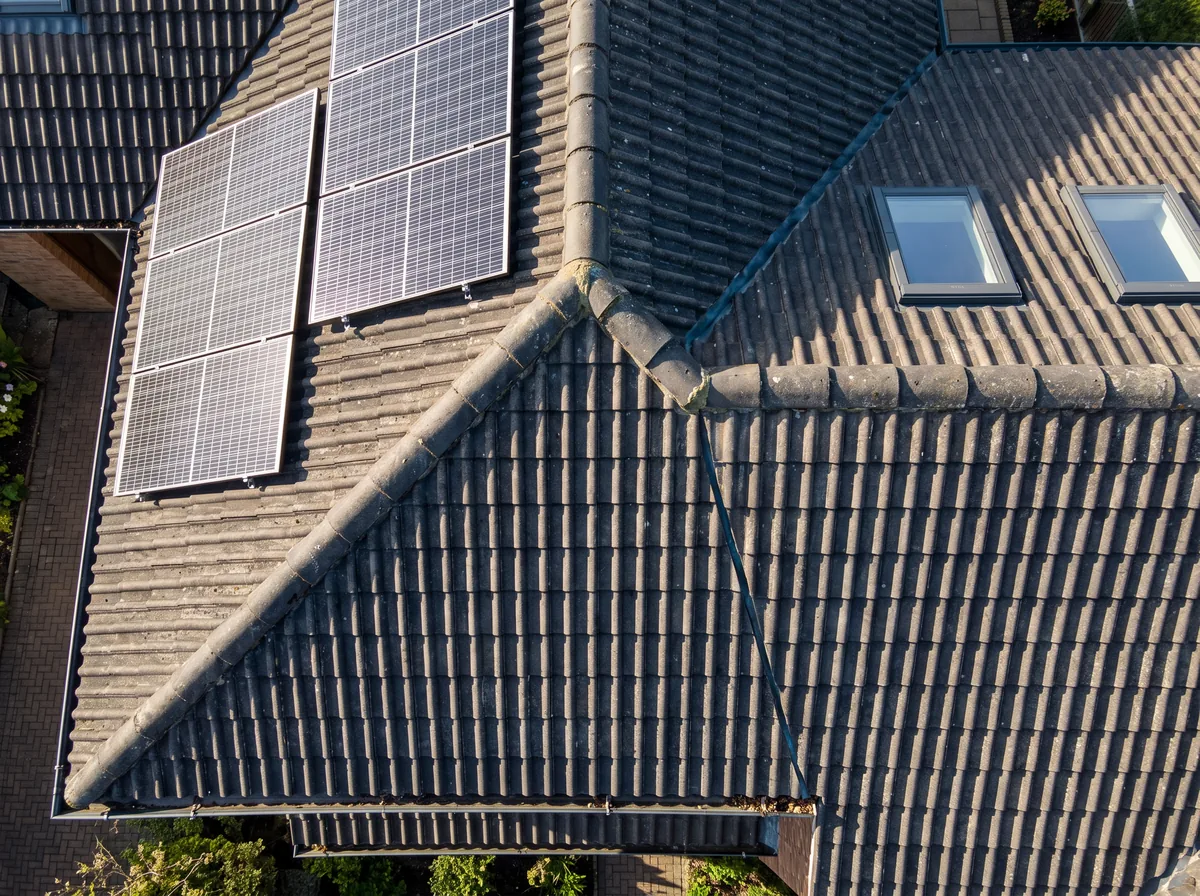 Detailaufnahme aus geringer Höhe: Ziegeldach mit Solarmodulen, Dachfenstern und klar erkennbarer Ziegelstruktur