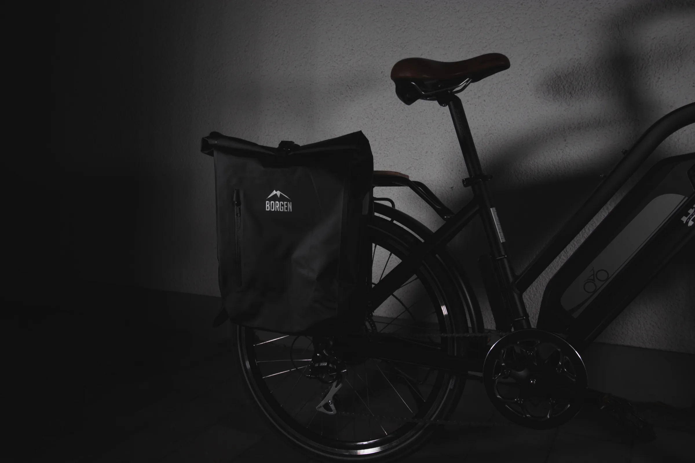 E-Bike mit schwarzer Gepäckträgertasche, im Streiflicht vor dunkler Wand aufgenommen