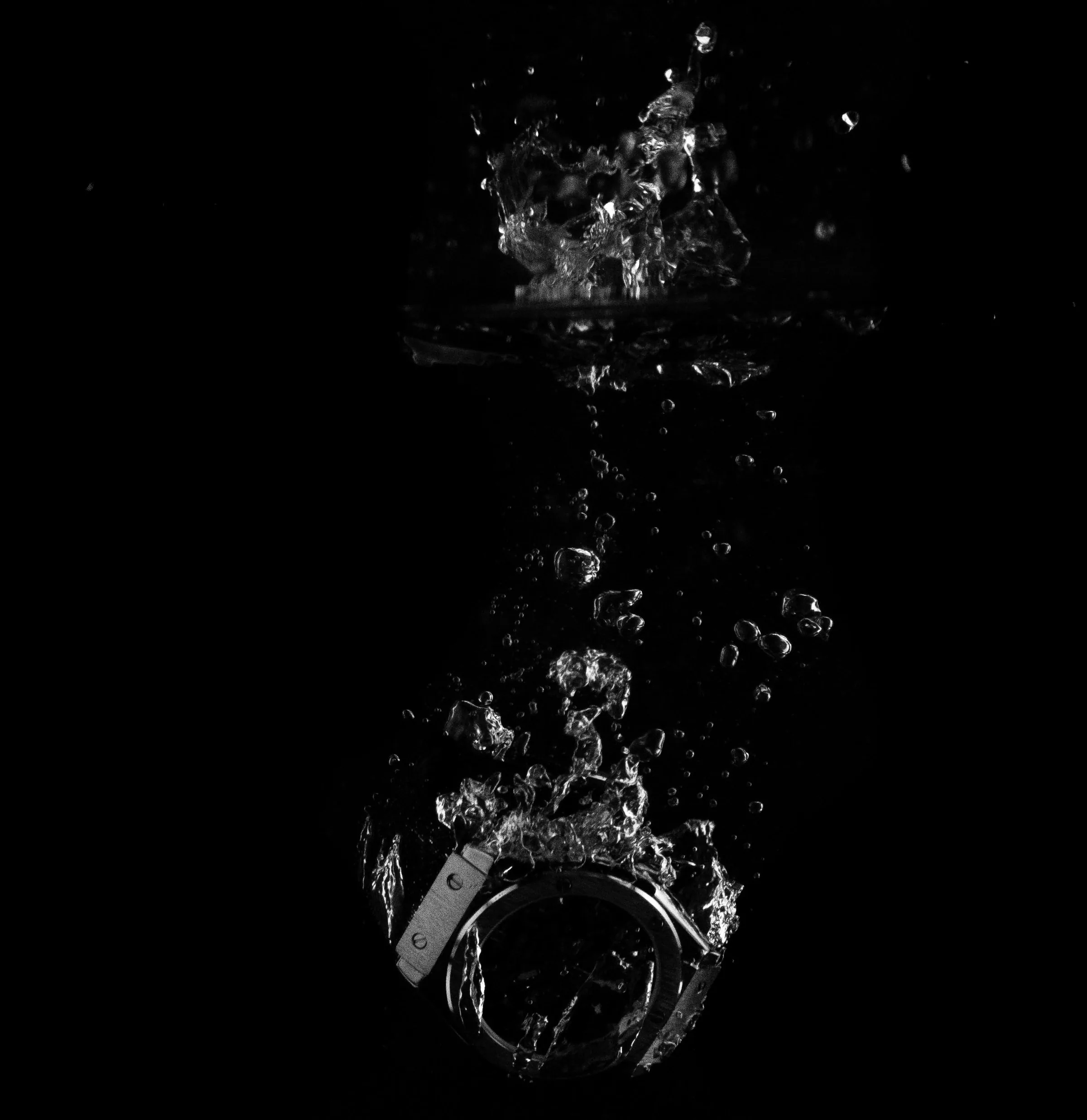 Armbanduhr taucht in Wasser ein, Luftblasen steigen vor schwarzem Grund auf