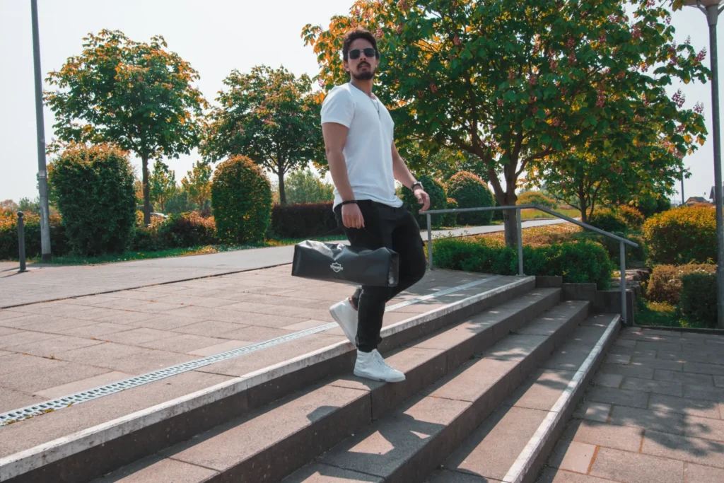 Mann mit einer Wheelo Tasche, die eine elektrische Rollermatte enthält, auf einer Treppe